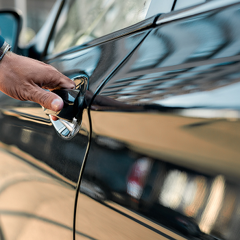 Cropped photo of a male hand opening the door of a black car while standing outdoors.